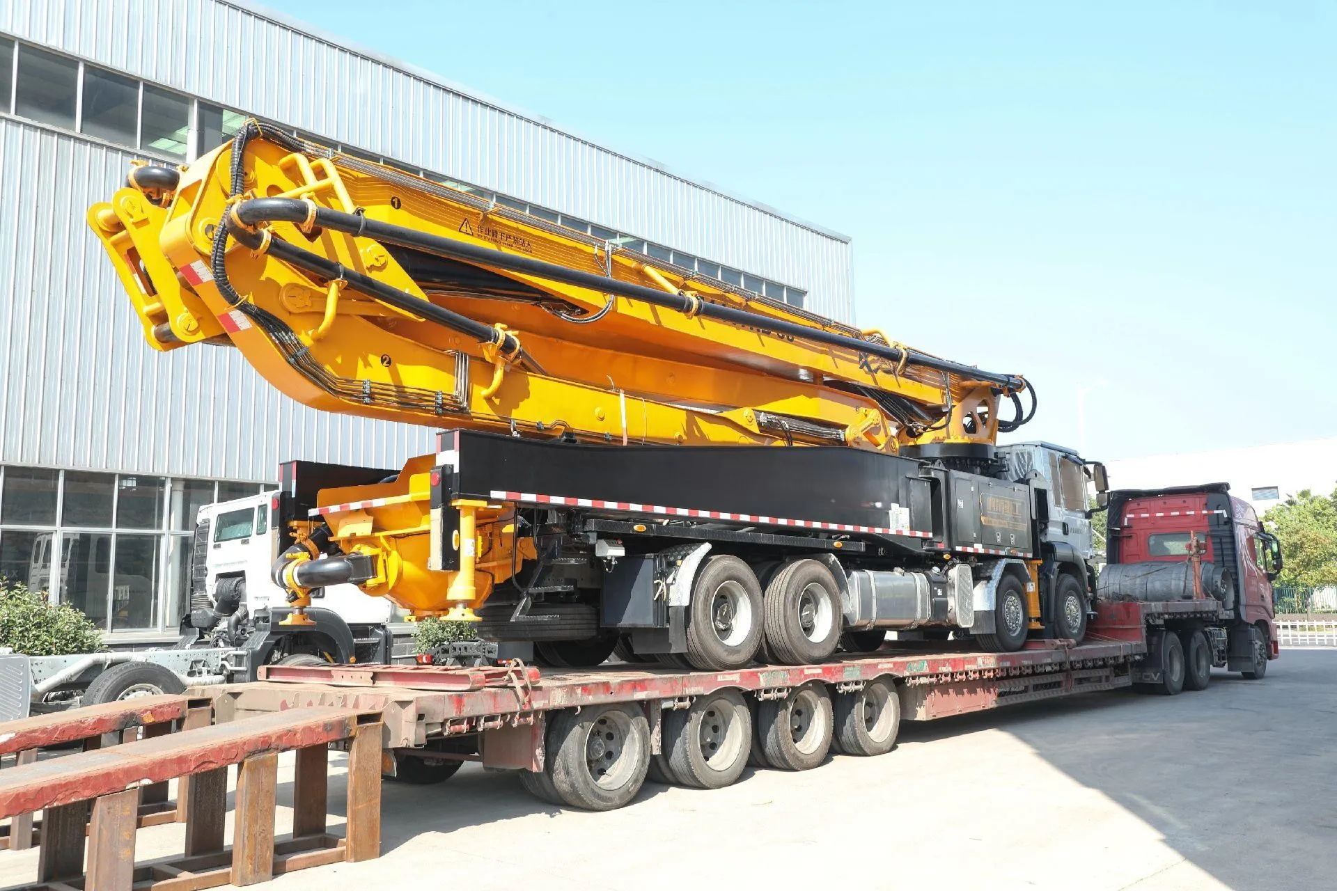 Concrete pump truck with yellow placing boom loaded on a lowbed trailer for export delivery