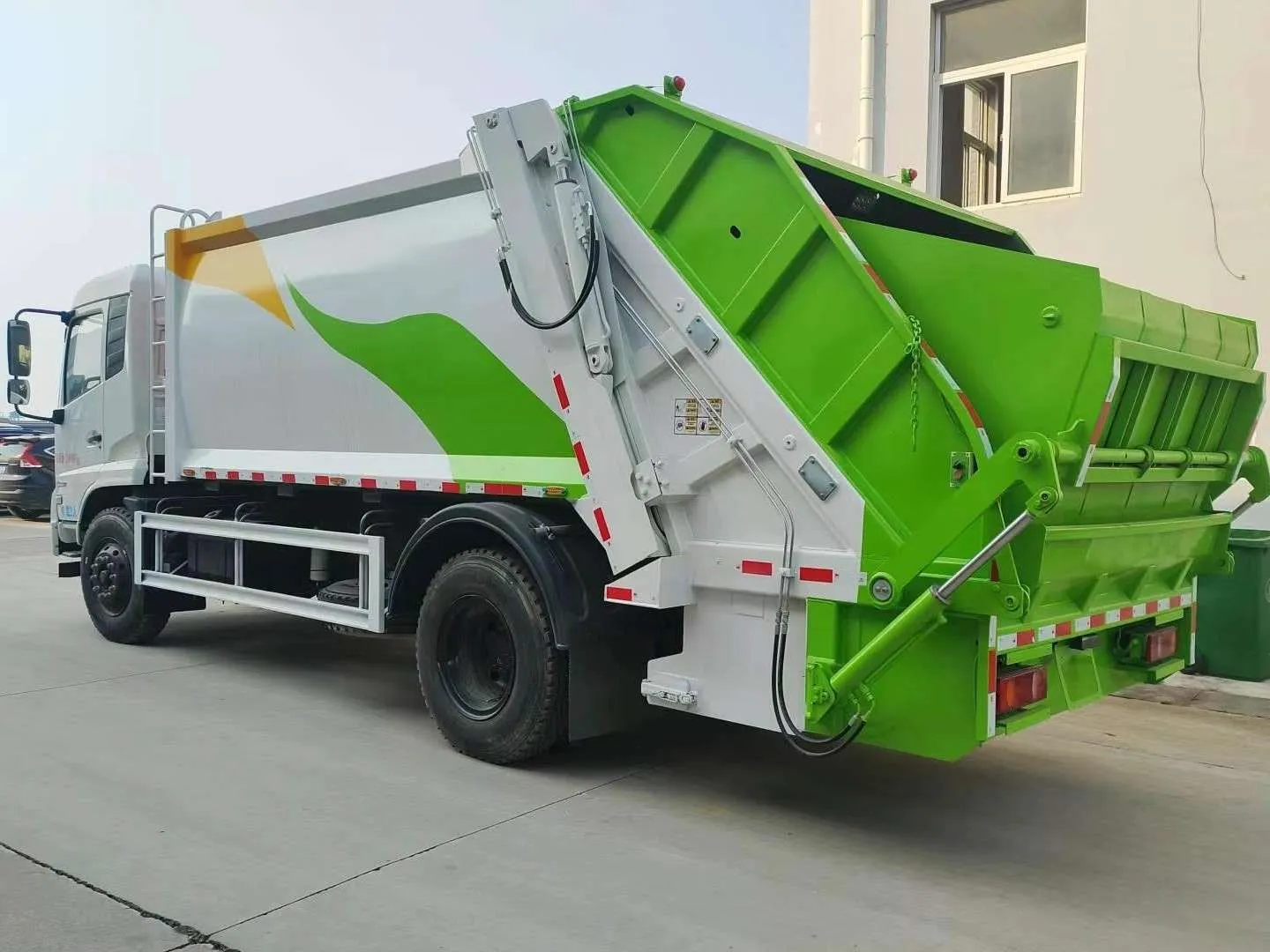 Rear-loader garbage compactor truck with the tailgate raised for discharge, showing the packer plate and hydraulic rams