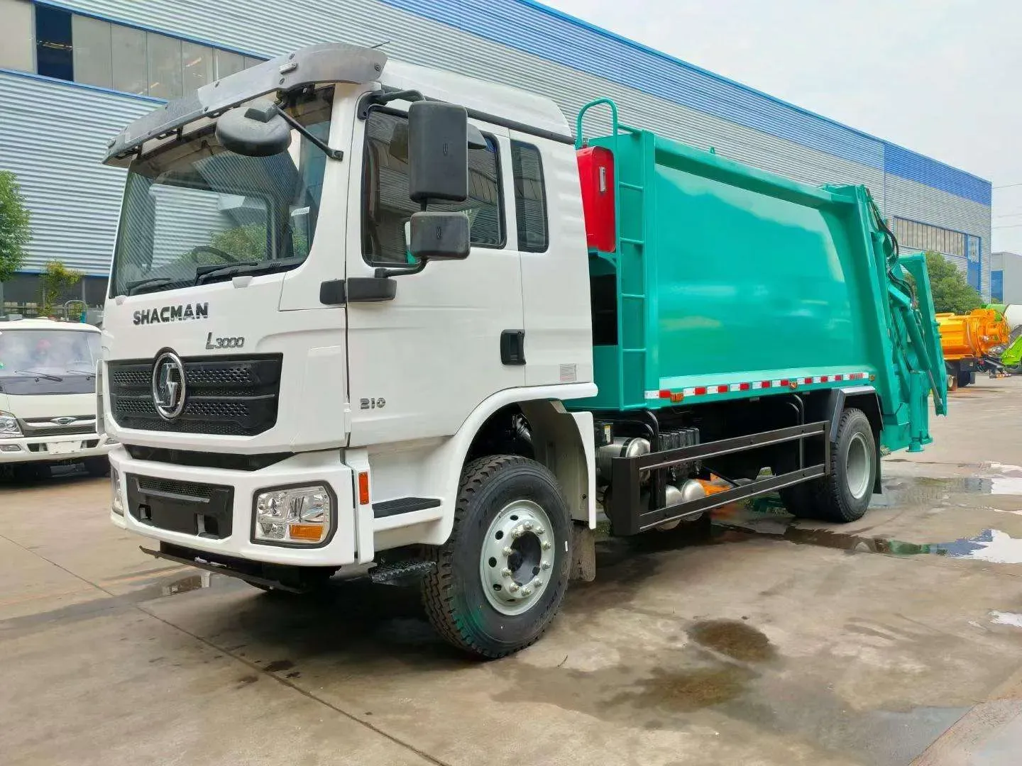 White Shacman rear-loader garbage compactor truck, front three-quarter view in the factory yard