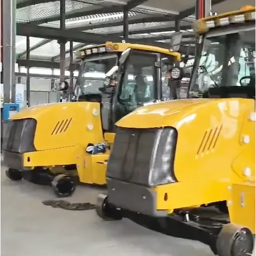 Two yellow ride-on industrial sweepers with enclosed cabs parked side by side inside a factory workshop