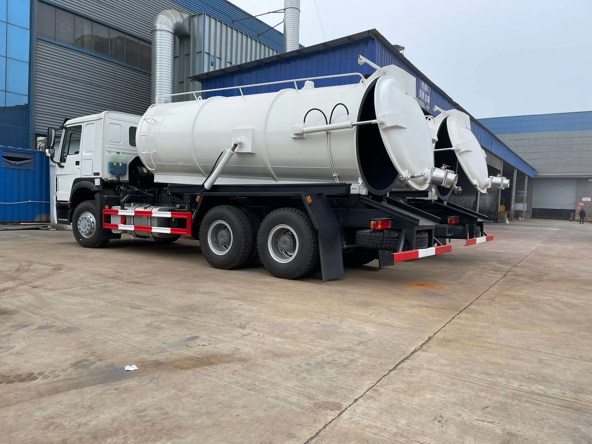 Sewage suction truck with the full-diameter rear tank door swung open, showing the discharge coupling