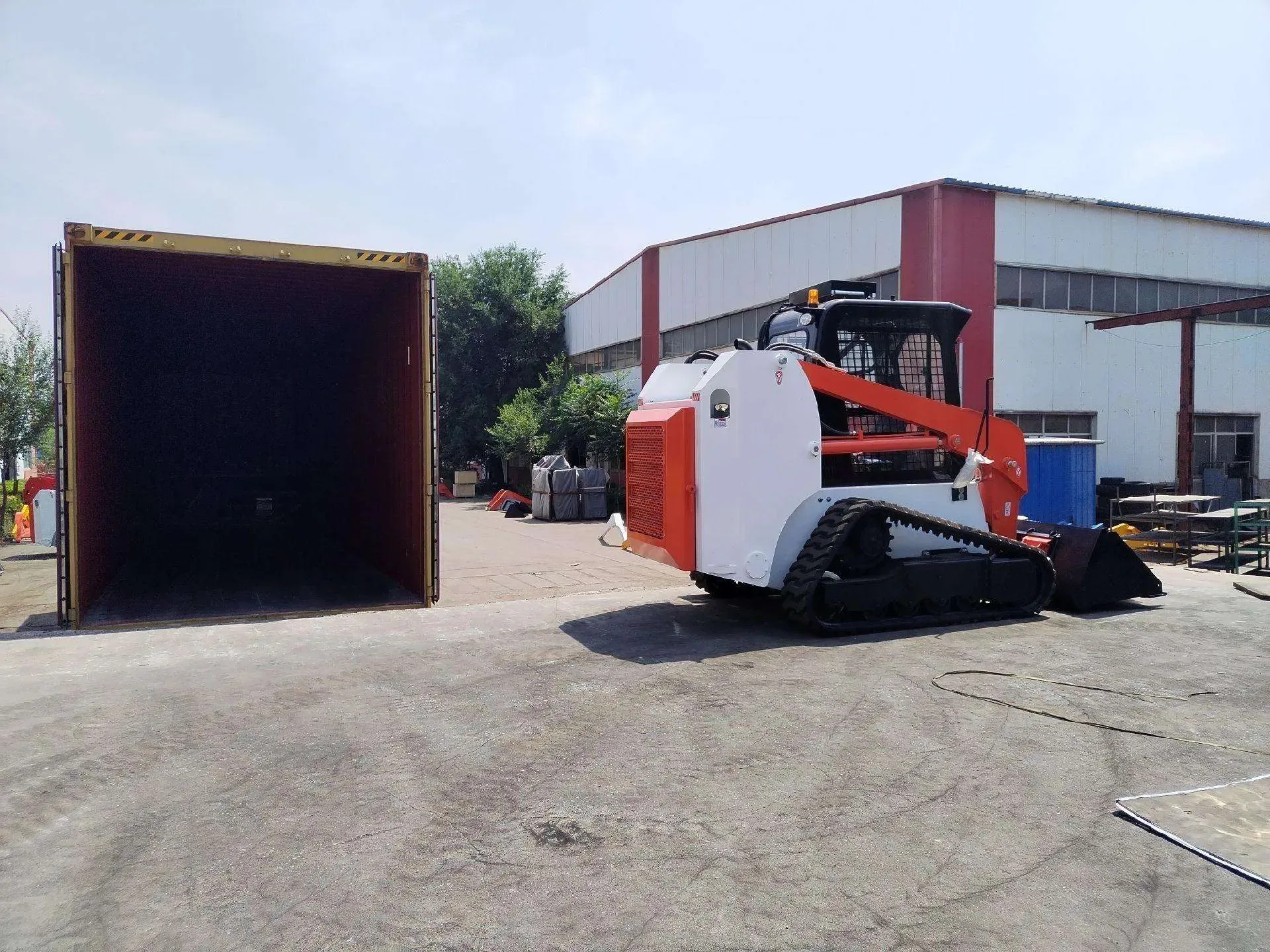 A tracked skid steer loader positioned beside an open container before loading